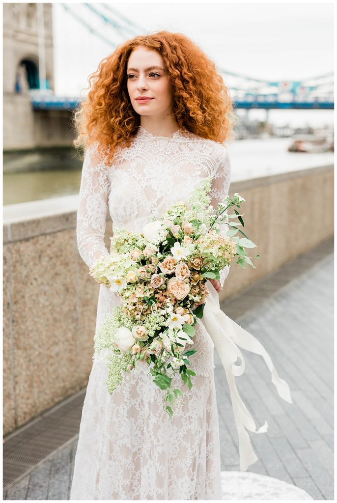 Bride in Claire Pettibone dress in front of Tower Bridge in London with a bouquet